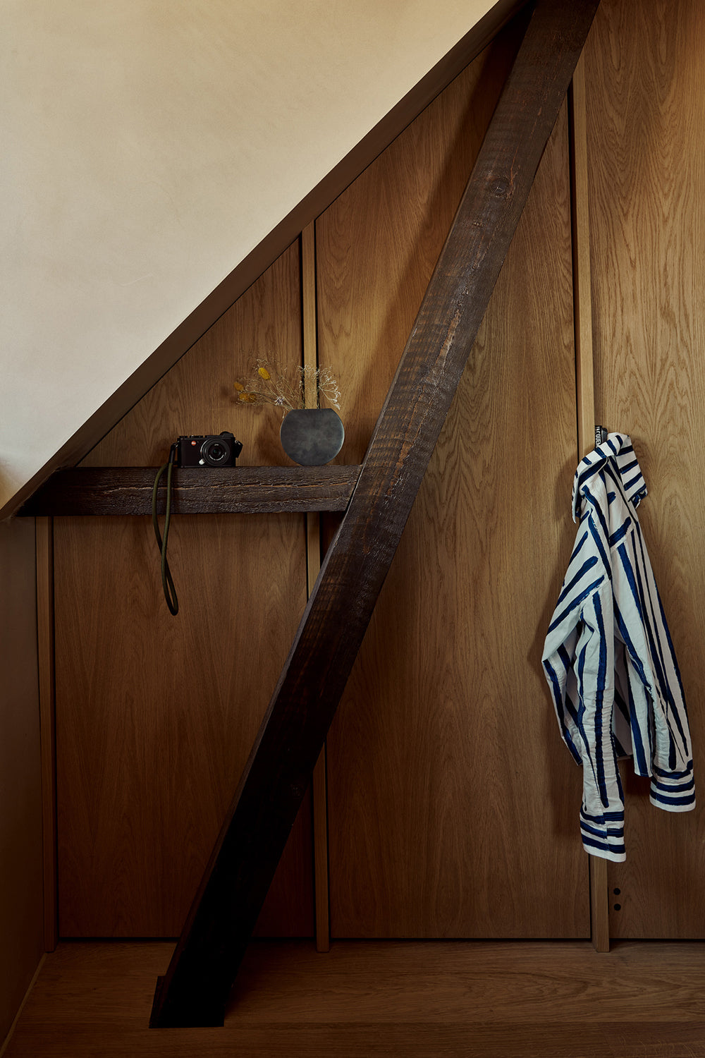 Oak-paneled nook with dark diagonal beam, shelf holding black camera and round