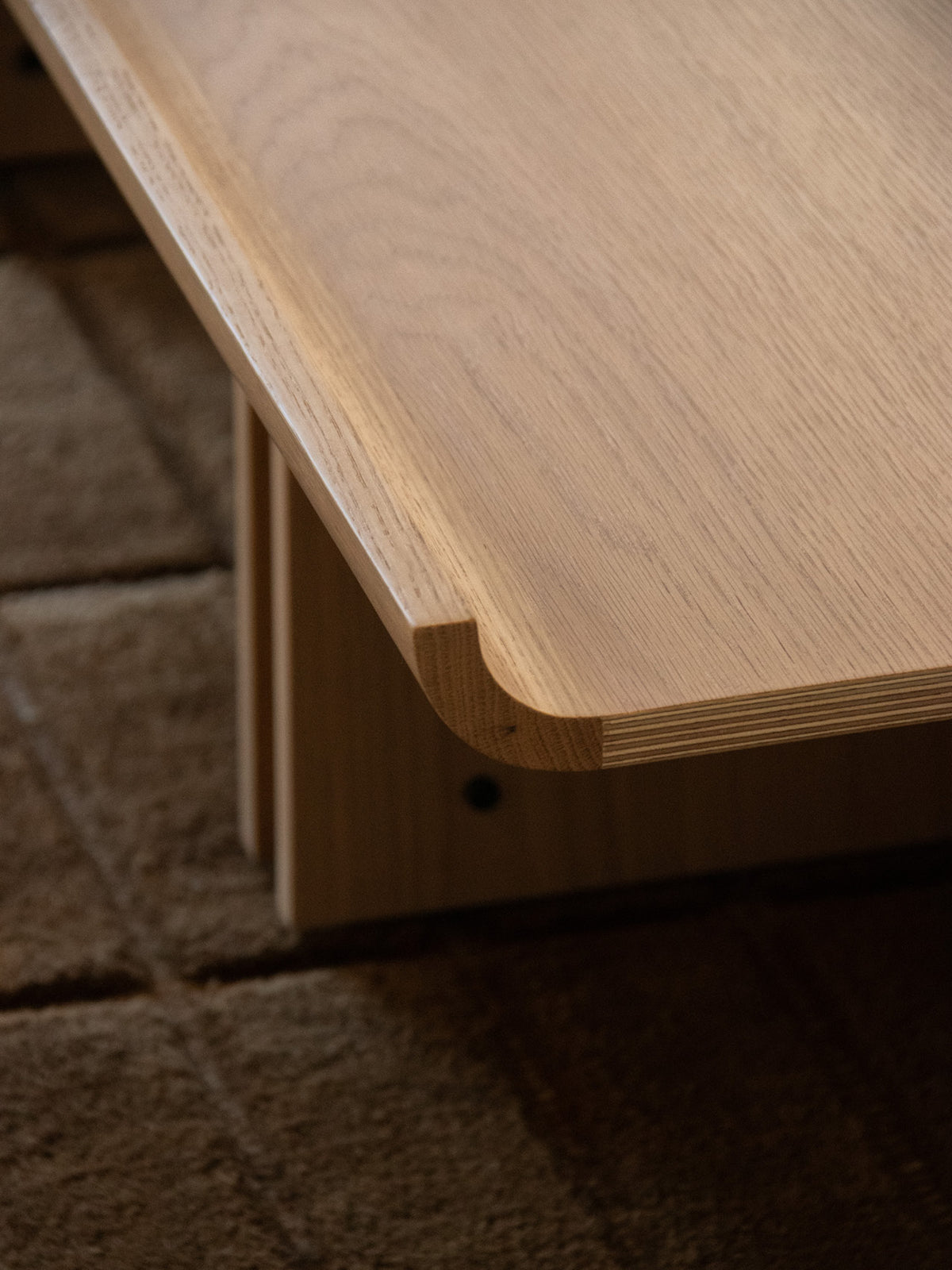 Light oak wooden table edge with rounded cutout detail, visible grain and