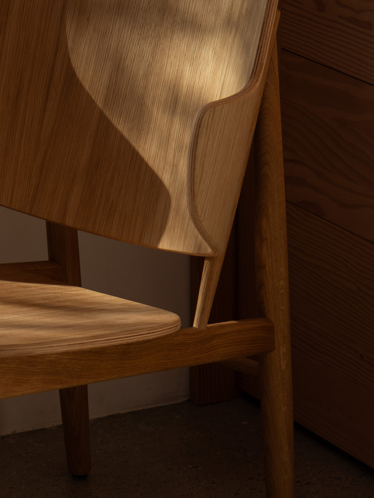 Close-up of a sculpted oak chair with curved backrest and rounded seat,