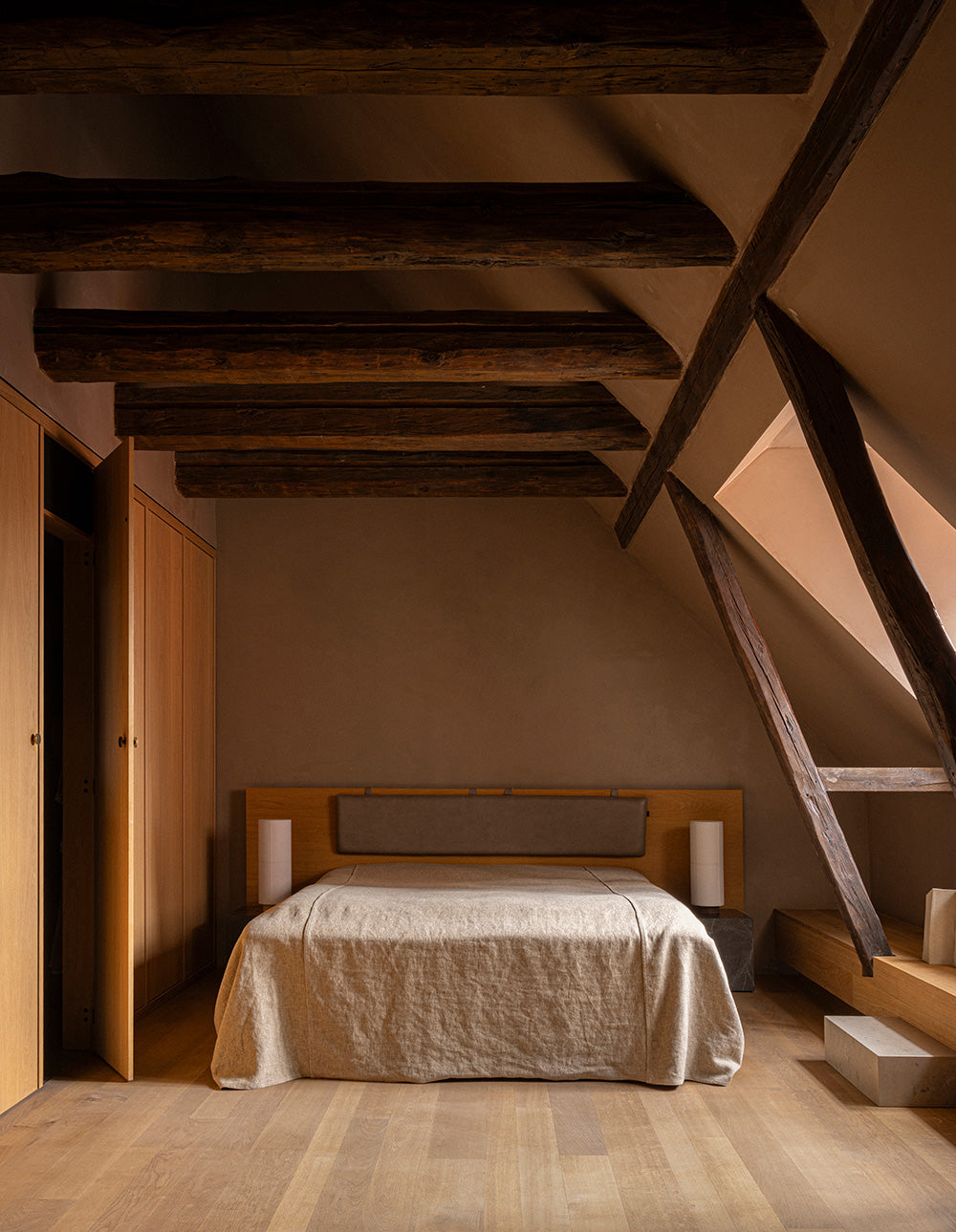 Minimal attic bedroom with oak bedframe, beige linen bedspread, exposed dark woo