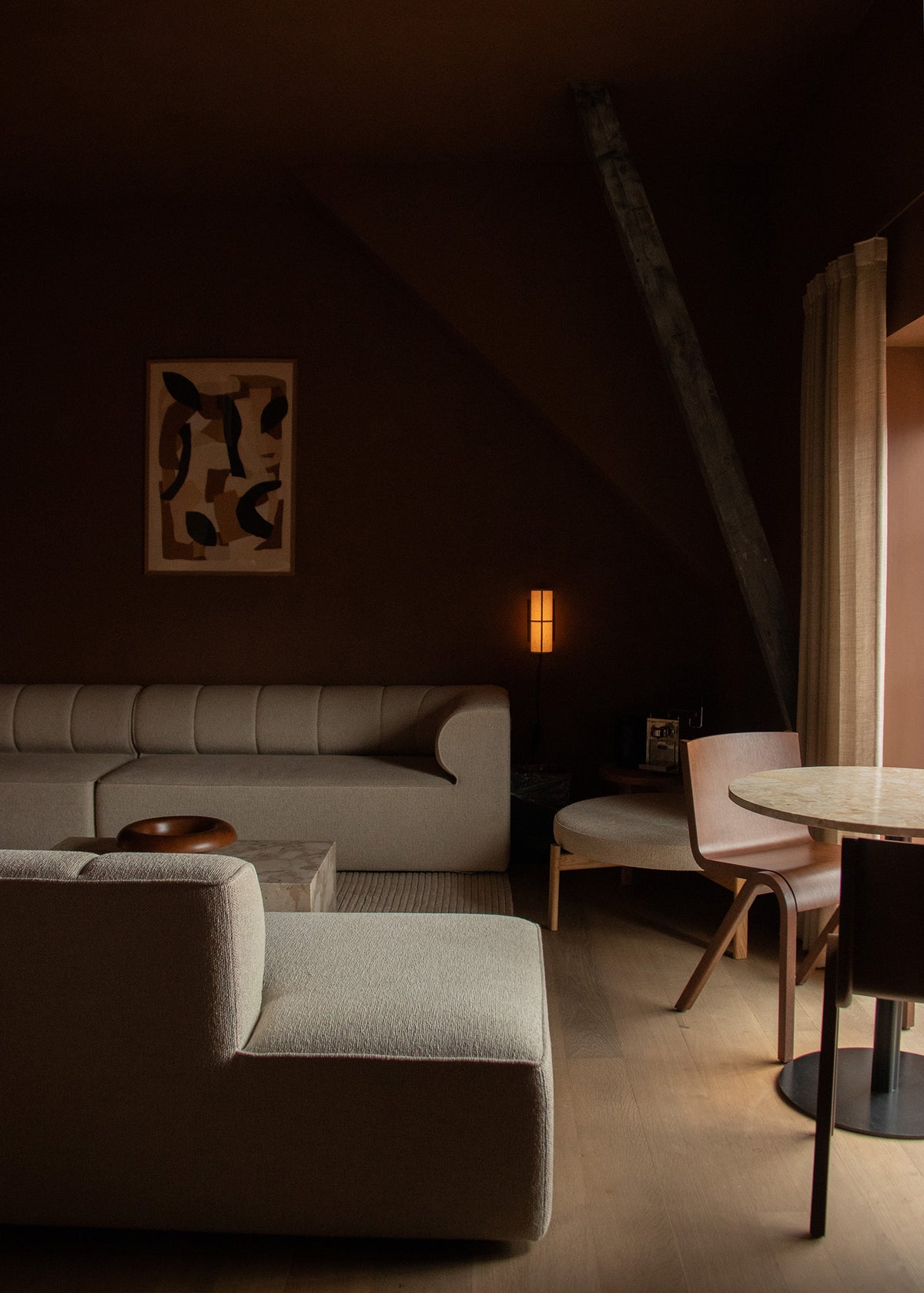 Warm, dim living room with beige upholstered sectional, round wooden chair and