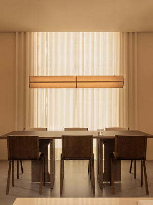The Hashira Linear Pendant Lamp illuminates an Androgyne Dining Table and Ready Dining Chairs in a serene, warmly lit room.
