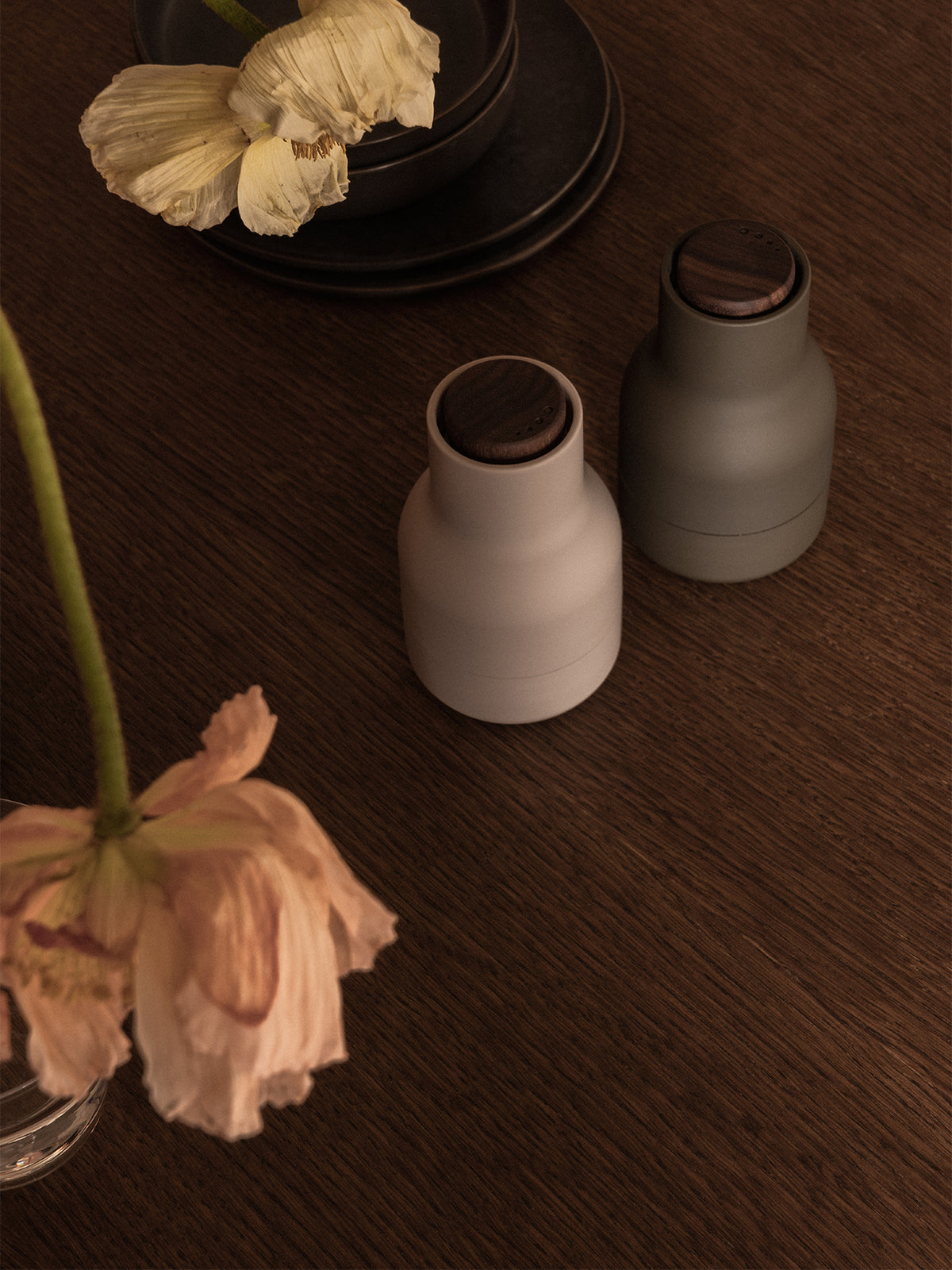 Zwei Audo Bottle Grinders in Beige und Dunkelgrün auf einem dunklen Holztisch