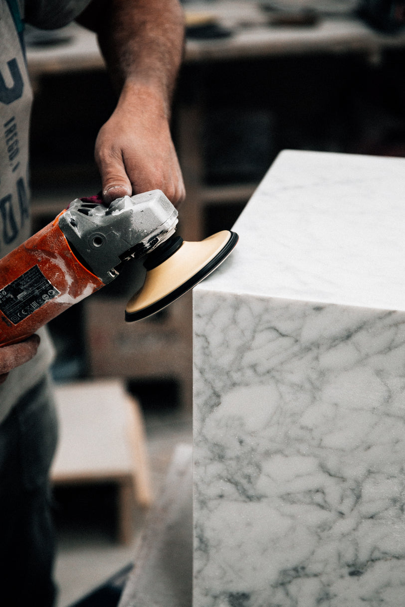 Hand-held polisher smoothing the sharp edge of a white marble block, close-up