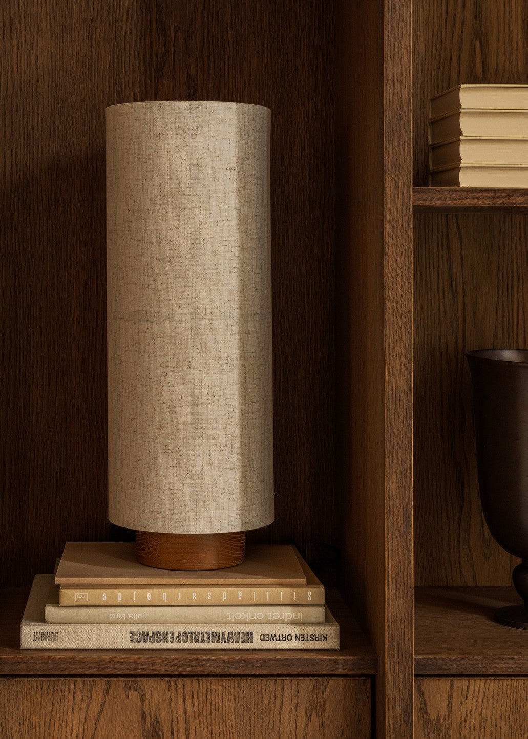 Beige cylindrical fabric table lamp with wooden base on stacked beige books