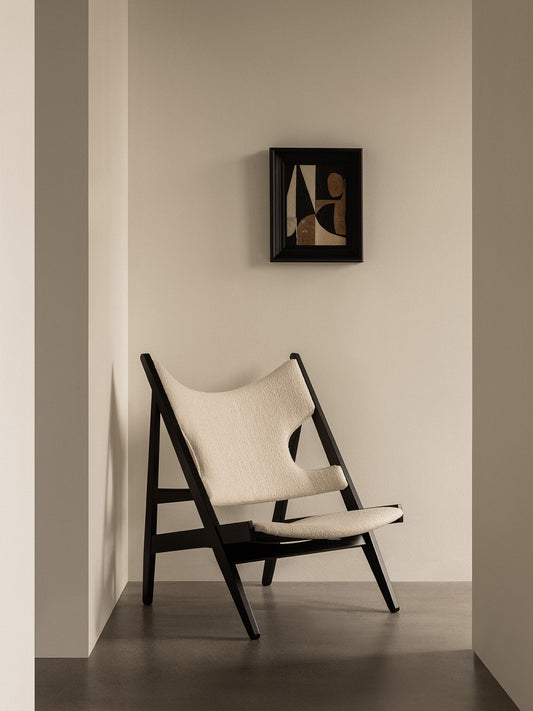 The image depicts a Knitting Lounge Chair with a black-stained solid oak base and ivory Barnum Bouéclé upholstery, displayed in a room setting with a framed picture on the wall.