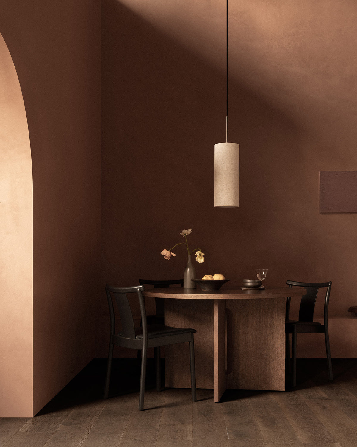 Minimal cylindrical beige pendant lamp above round wooden dining table with vase