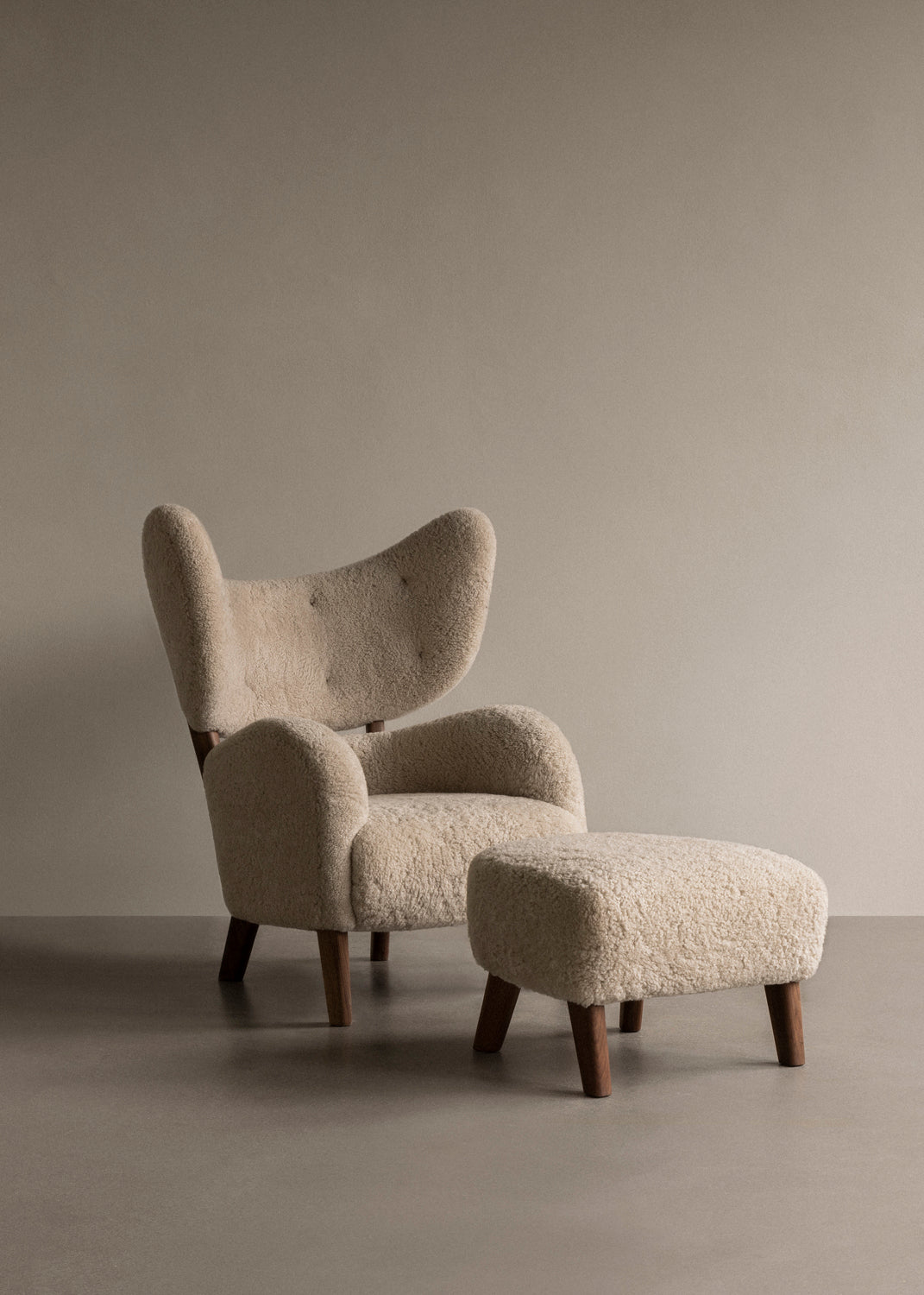 Beige boucle upholstered winged lounge chair with rounded arms and matching otto