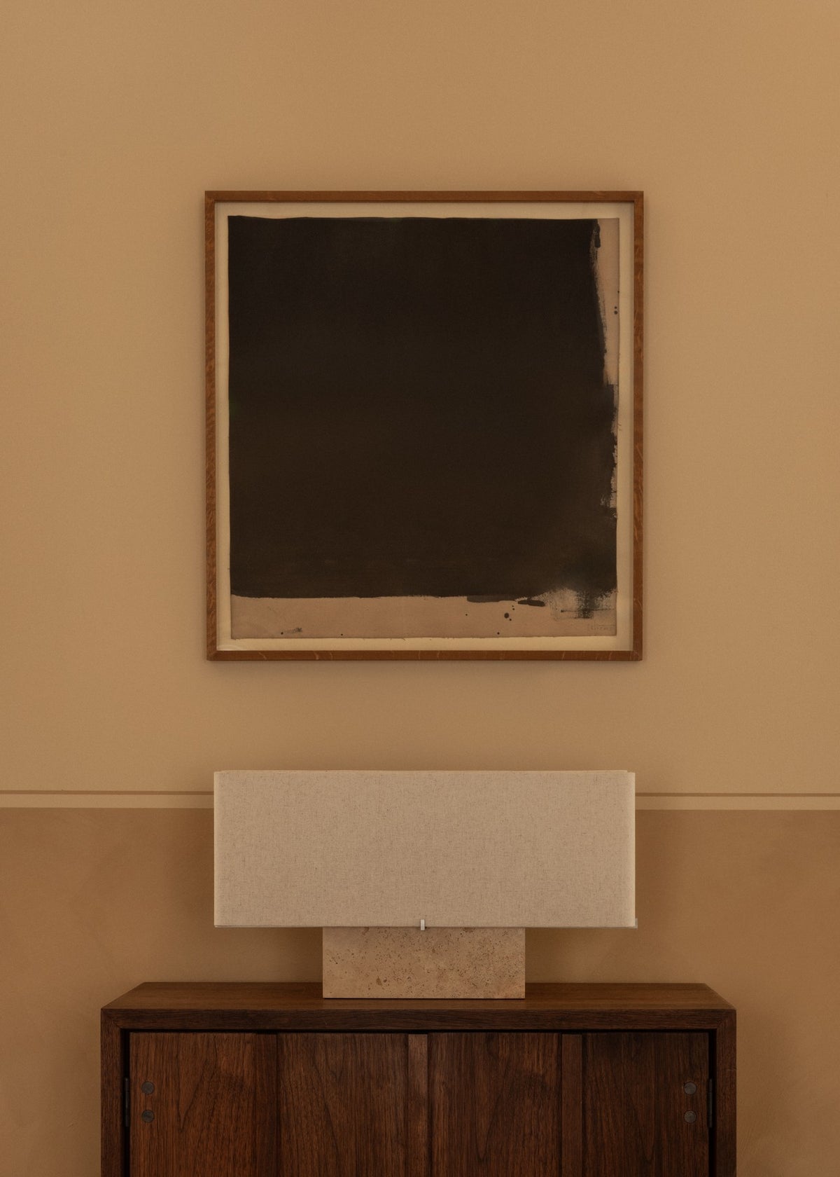 Minimalist black abstract painting in wooden frame above beige rectangular fabri