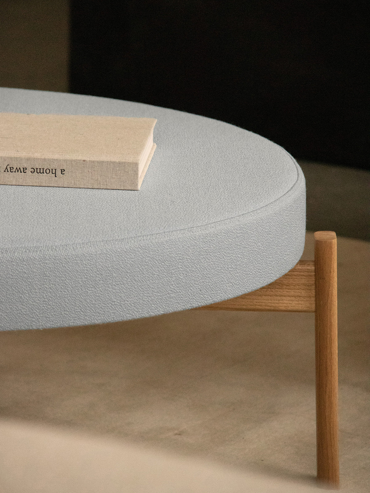 A close-up of the Passage Pouf's light grey textured fabric top and