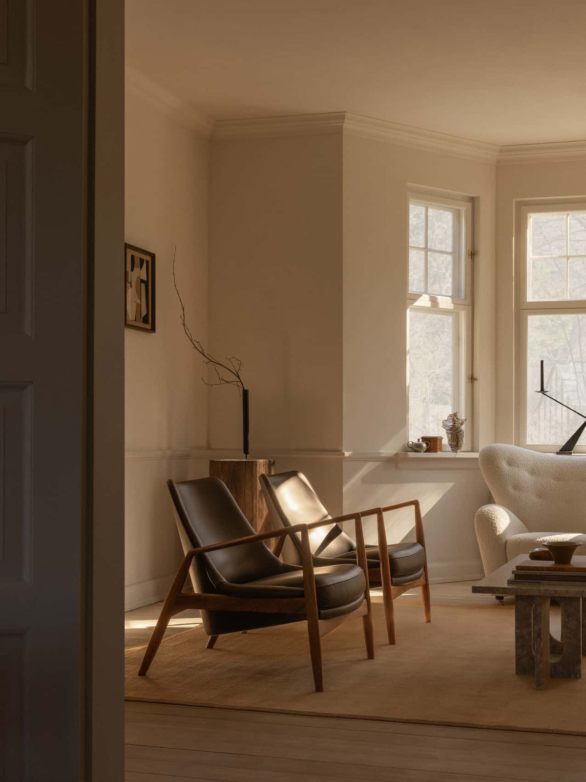 Sunlit living room with two dark leather and walnut lounge chairs, cream