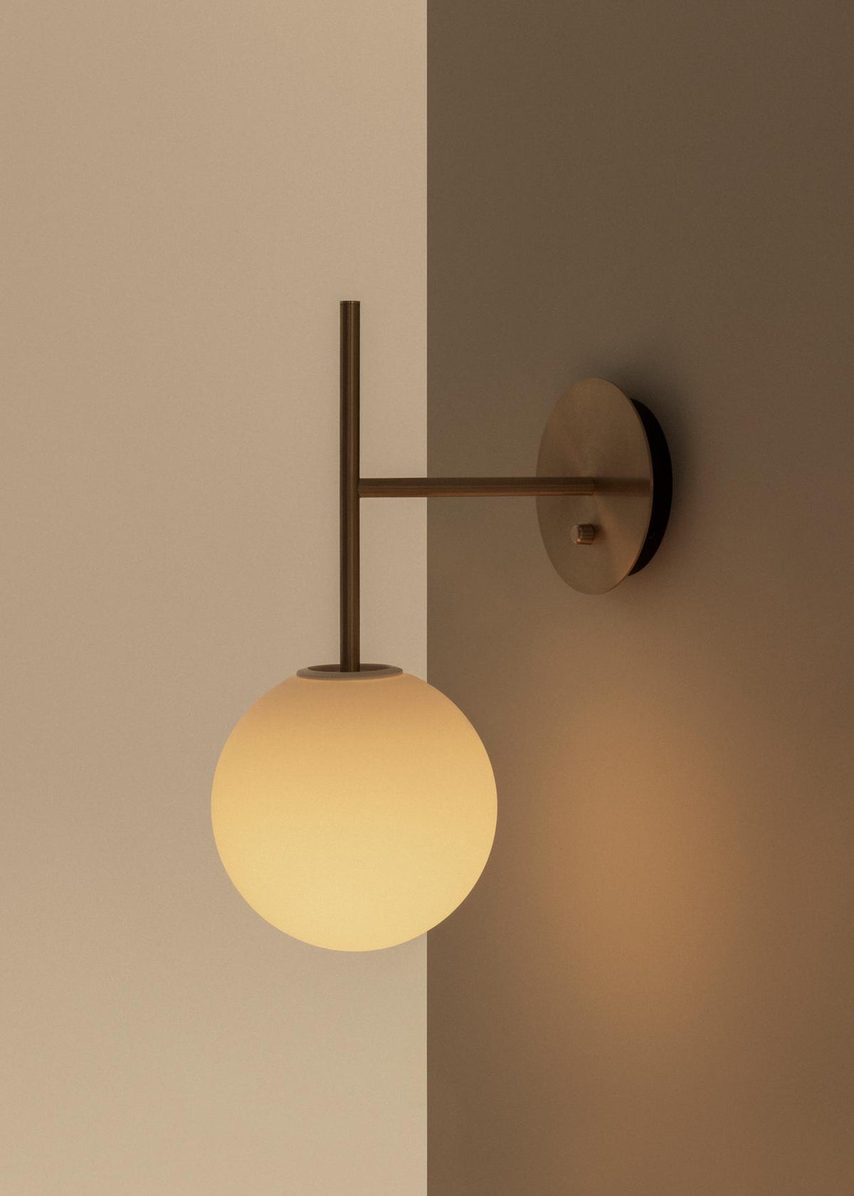 Brass wall sconce with vertical rod and frosted glass globe shade, warm