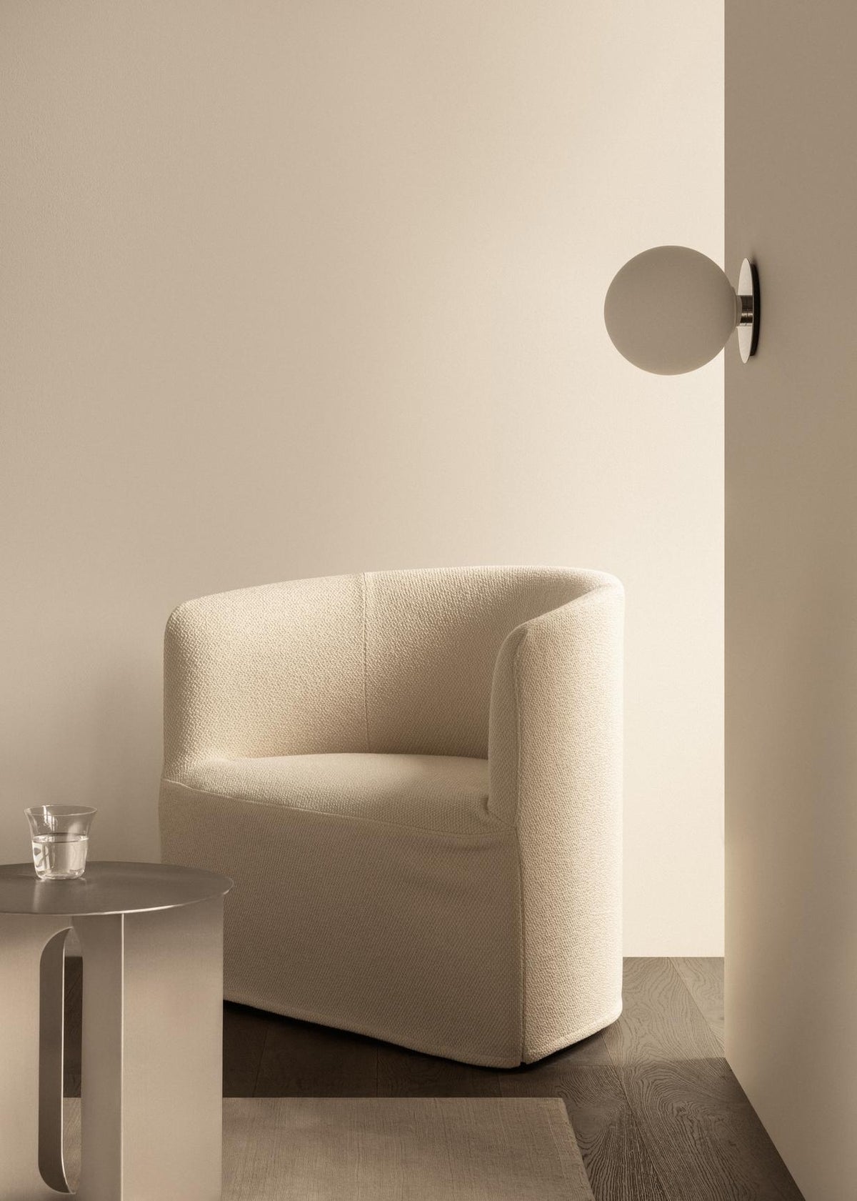 Cream boucle upholstered curved armchair beside round white wall sconce, small t