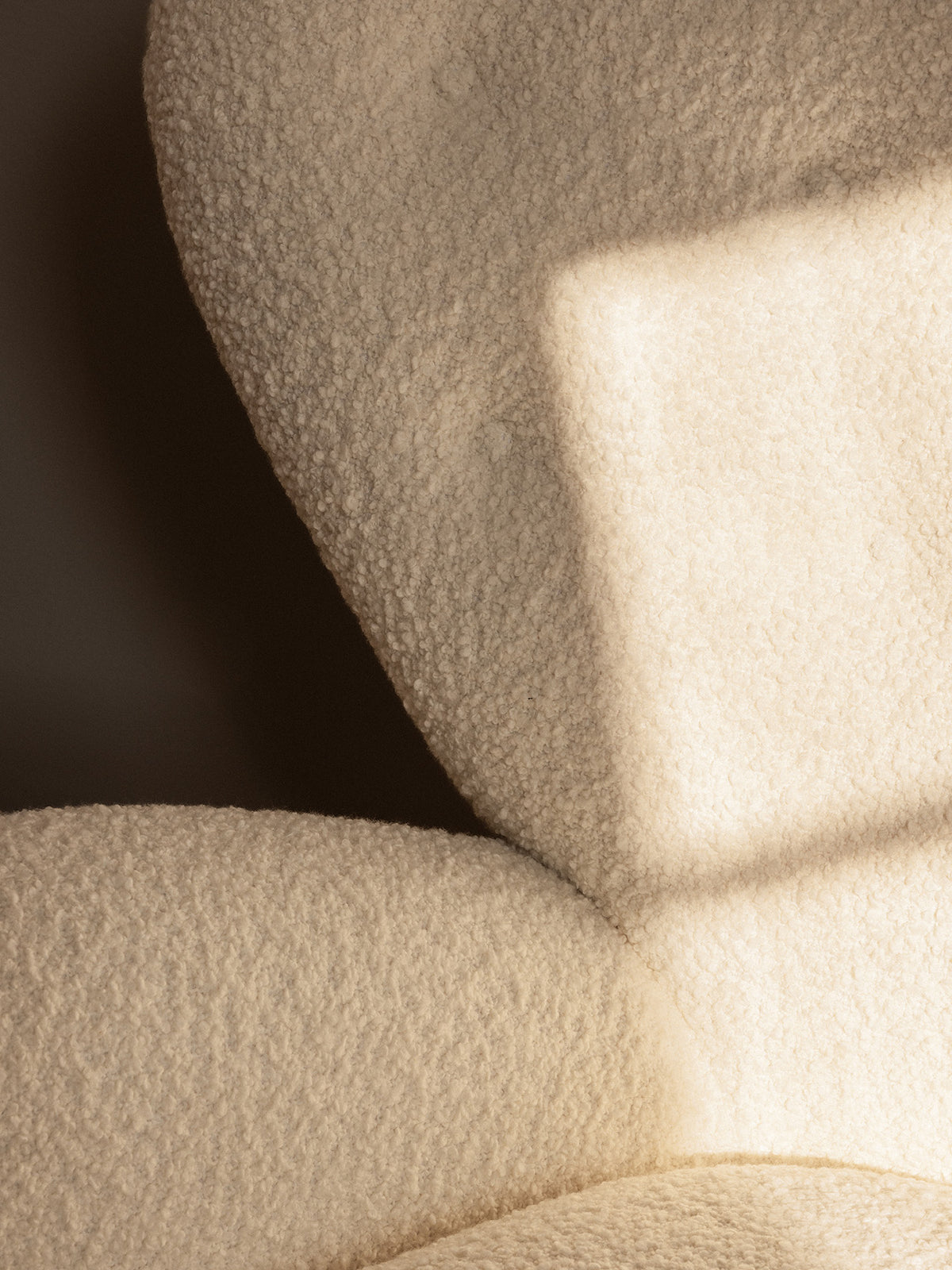 Close-up of a cream boucle upholstered chair showing curved cushions, textured w