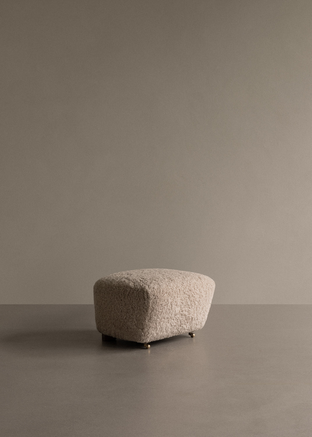 Beige boucle upholstered ottoman with rounded rectangular shape and small brass