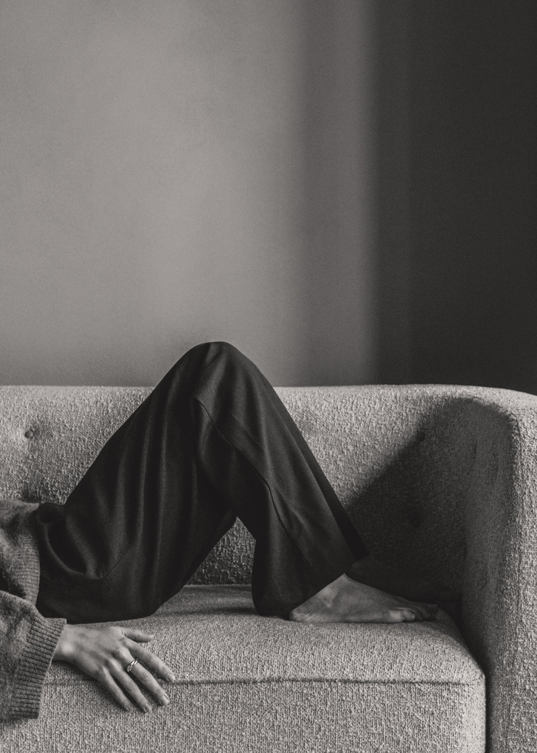 Black-and-white photo of a textured light-grey bouclé sofa with a person reclini