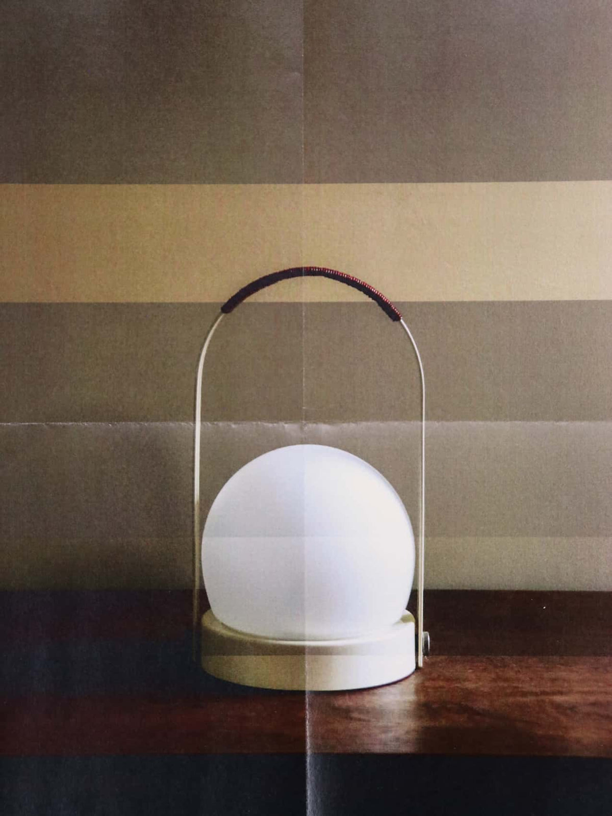 White spherical lamp on a round cream base with thin metal handle
