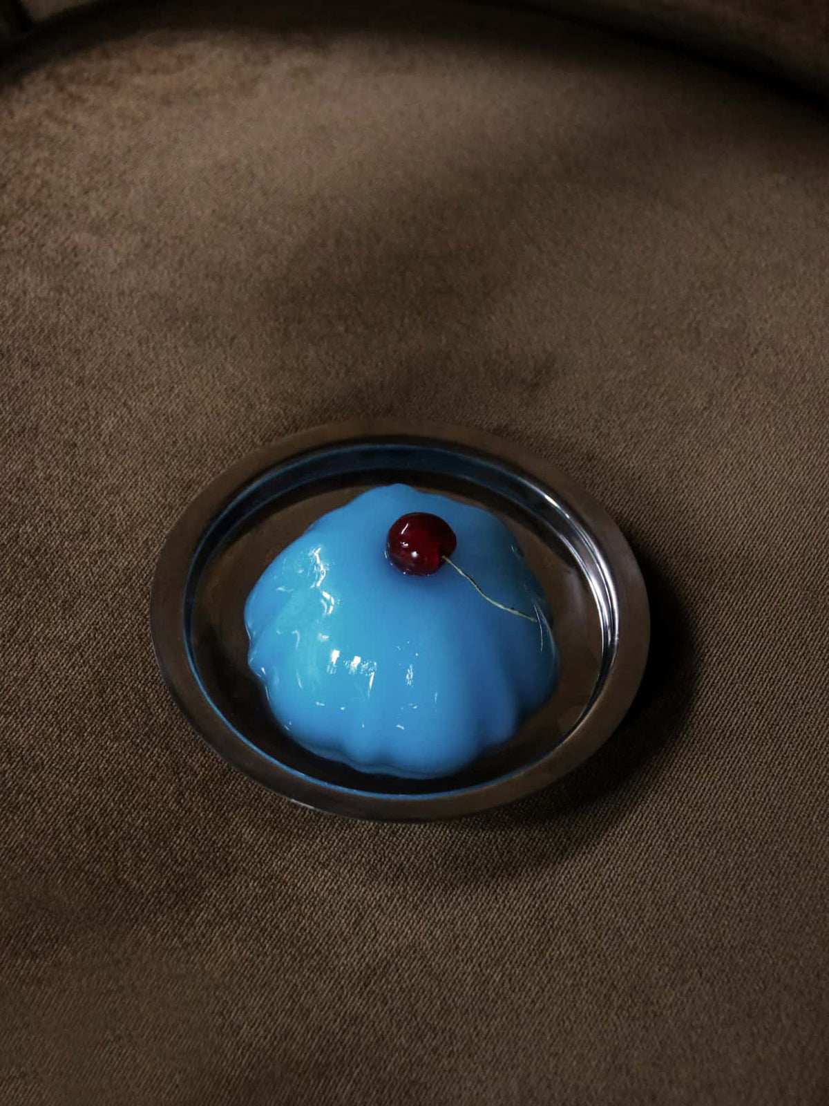 Glossy blue dome-shaped dessert with a red cherry on top, on a