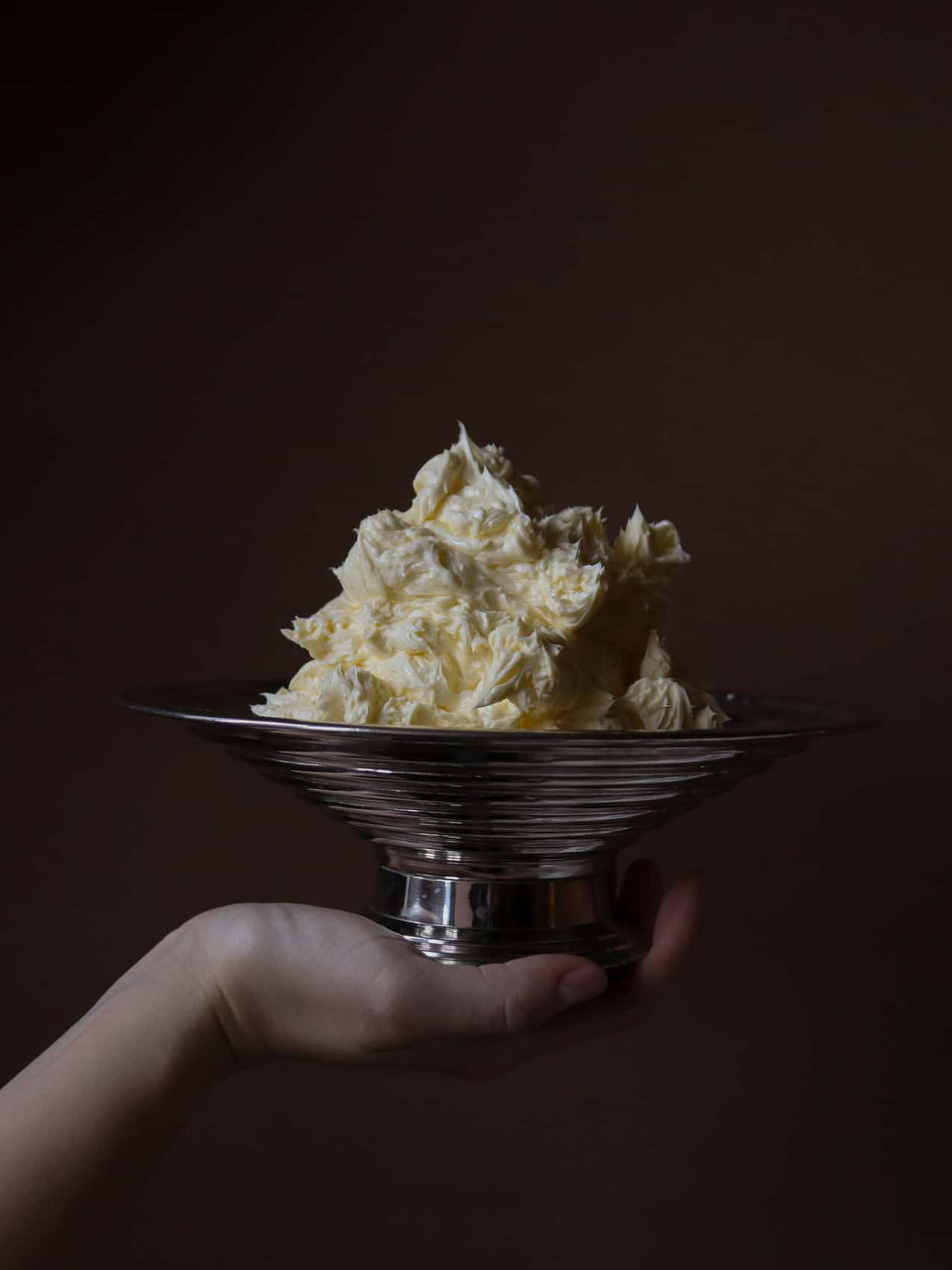 Shiny ribbed silver pedestal bowl held in hand with a creamy pale