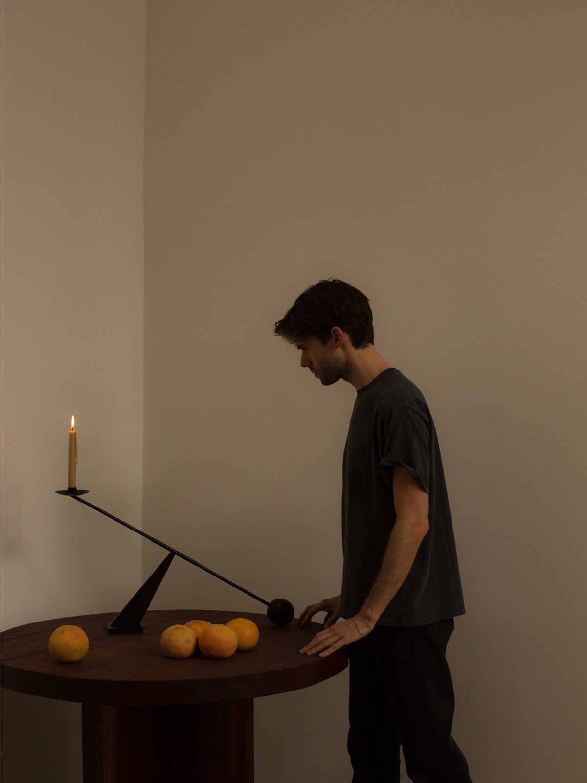 Minimal black metal seesaw candleholder on round dark wood table with lit