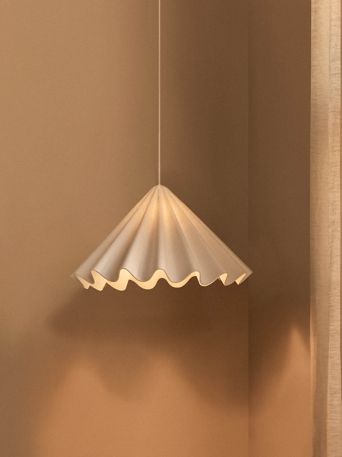 Cream pleated pendant lamp with scalloped wavy edge, suspended by cord against