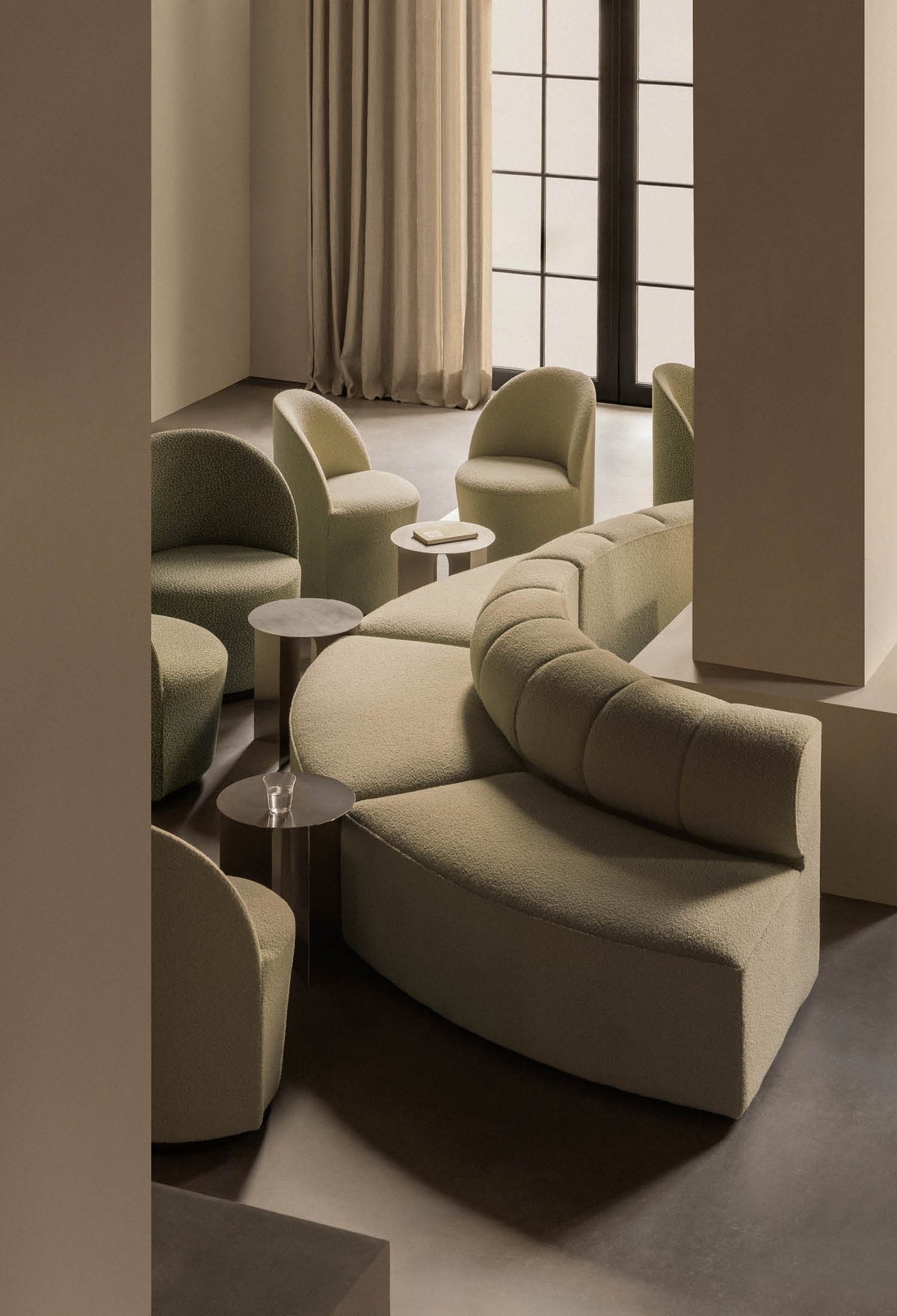 Minimalist seating arrangement with curved, olive-green boucle sofas and round s