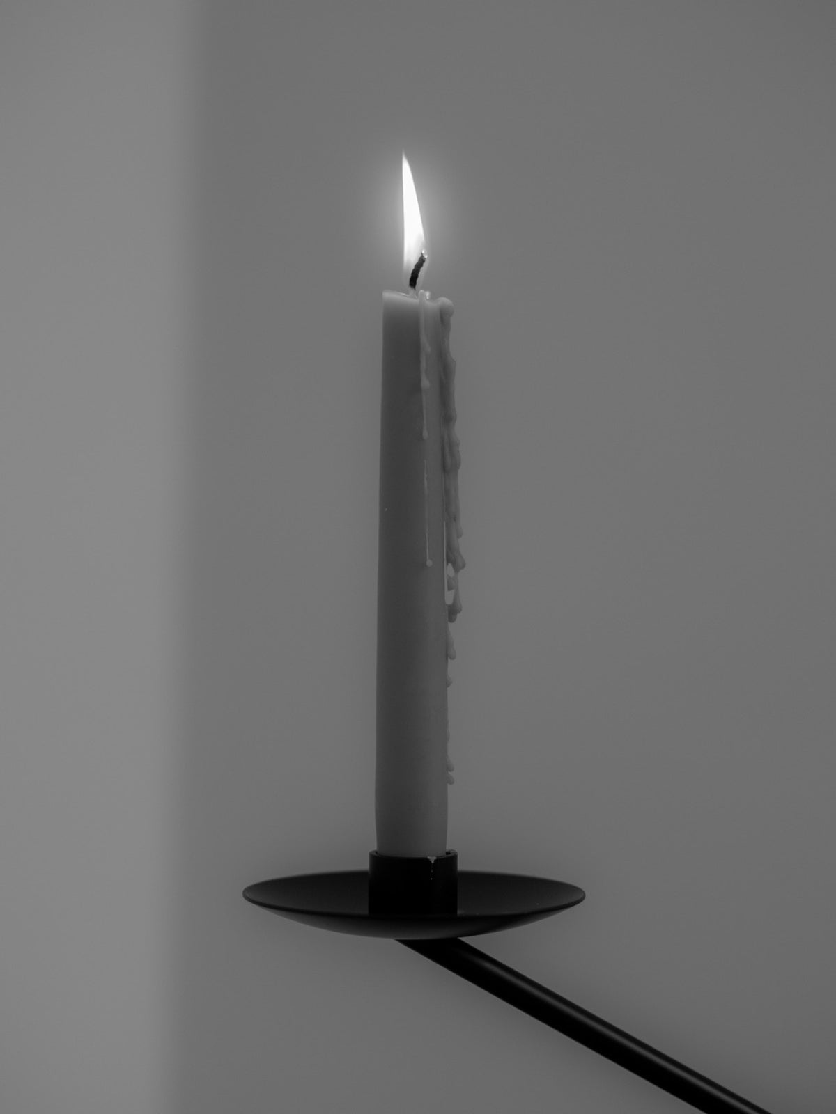 Tall lit tapered candle with dripped wax on a black metal wall-mounted
