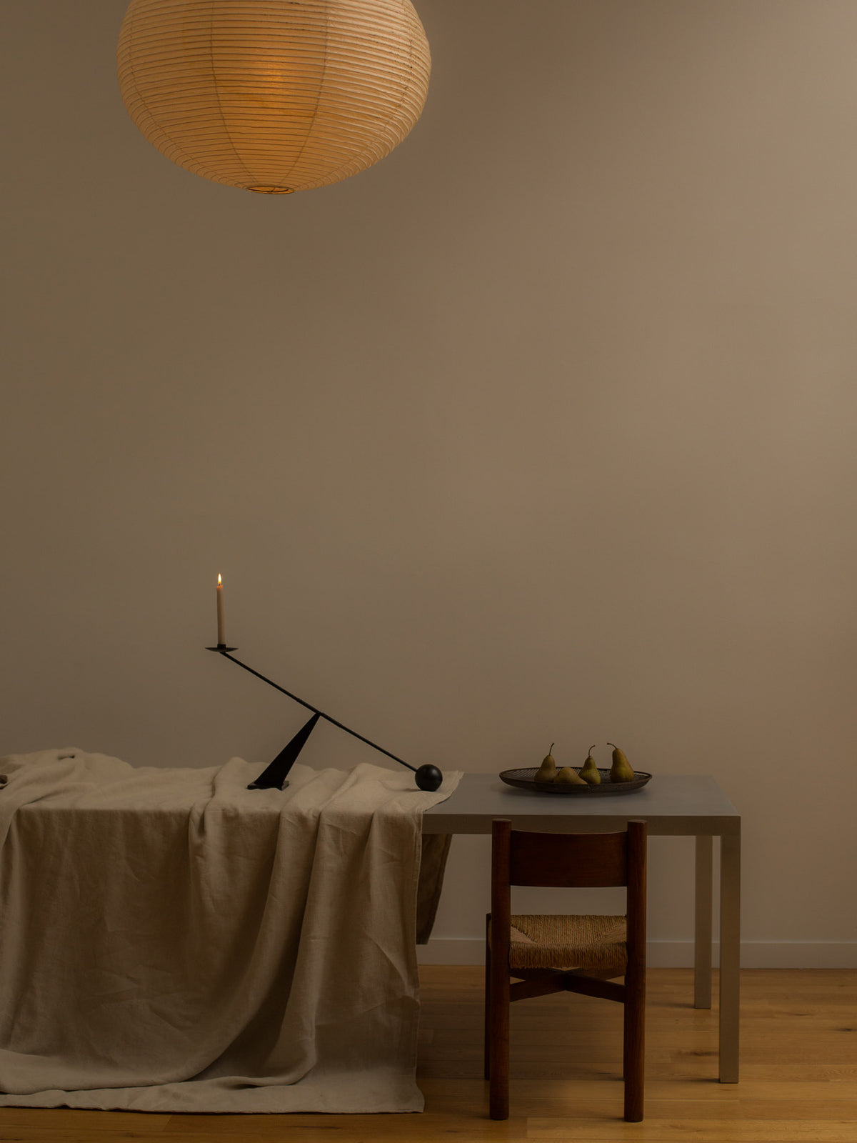 Minimal dining scene with linen-draped table, wooden chair, black balancing cand