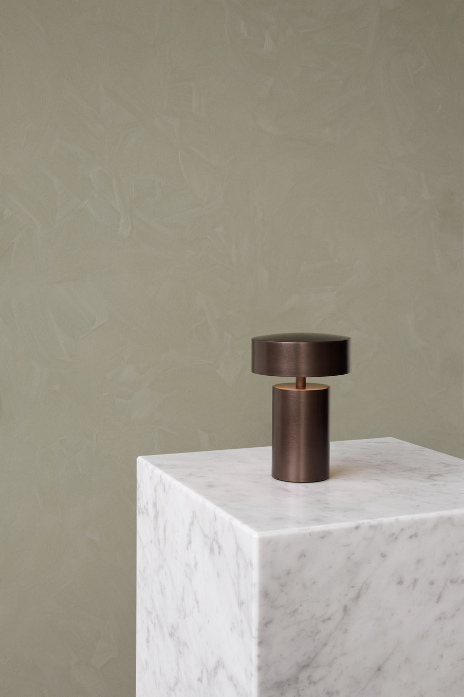 Small cylindrical bronze table lamp with round flat shade on white marble