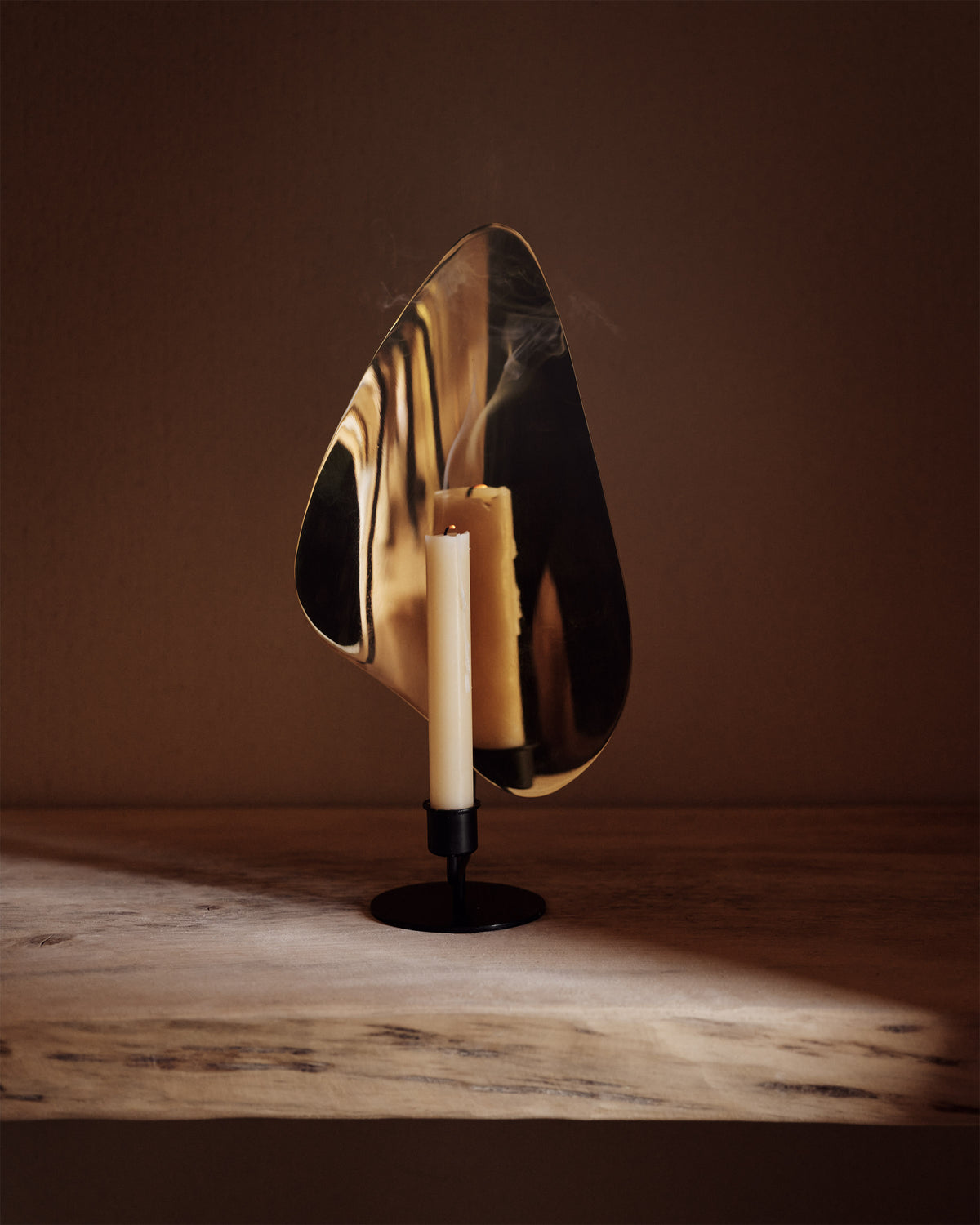 Brass curved reflector candleholder with black metal base and a lit white