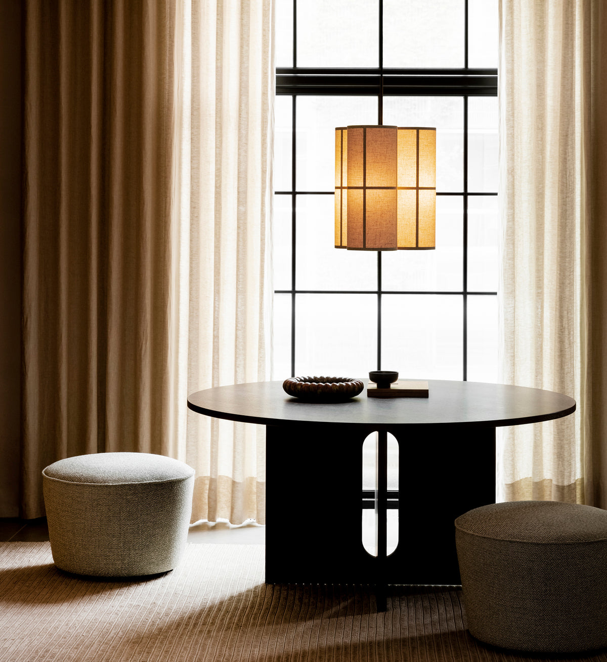 Round black wood table with sculptural base, beige fabric pendant lamp above,