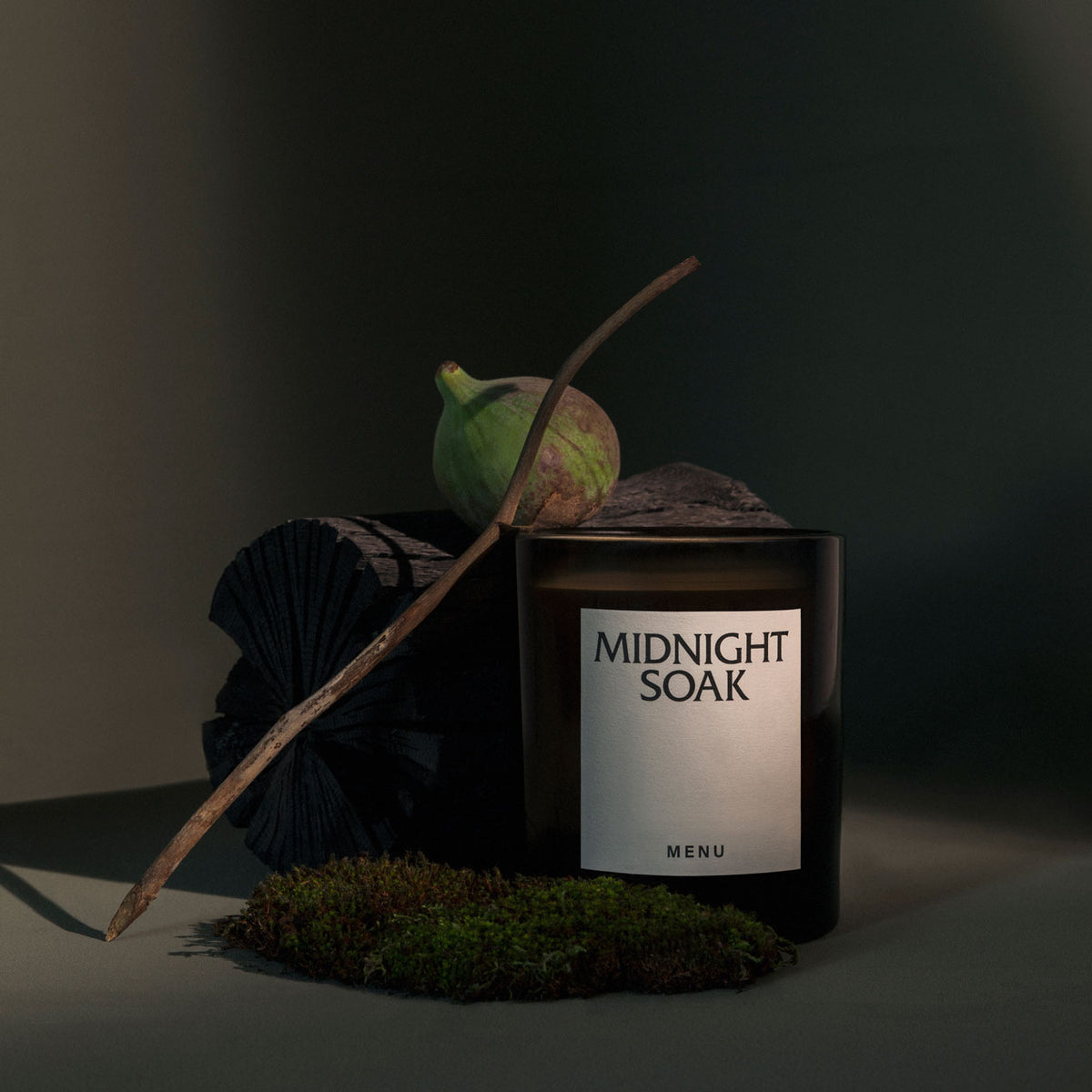 Dark amber glass candle labeled "MIDNIGHT SOAK" next to fig, twig, moss