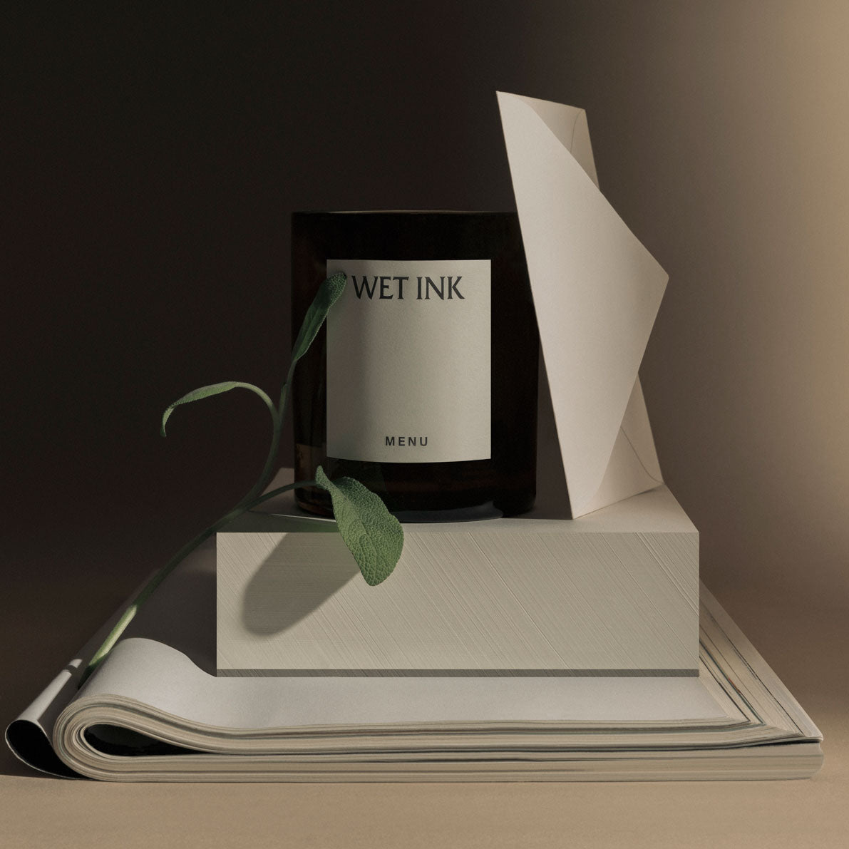 Amber glass candle labeled "WET INK" on stacked cream books and folded