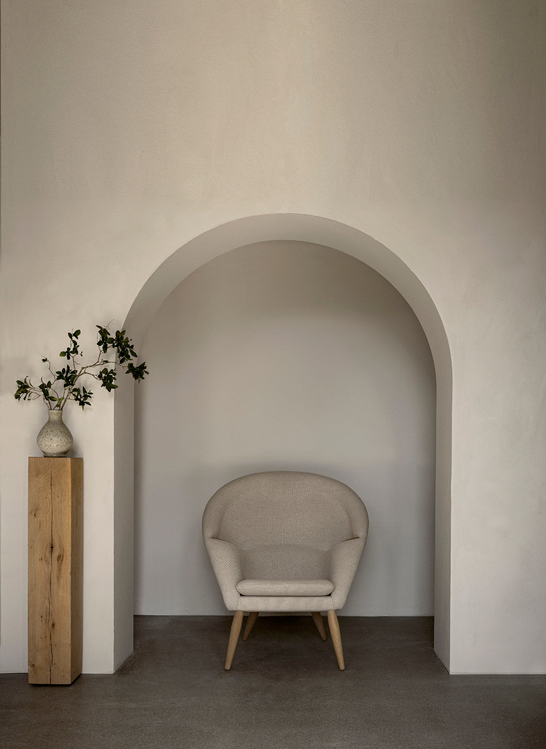 Beige upholstered rounded lounge chair with wooden legs set inside a pale