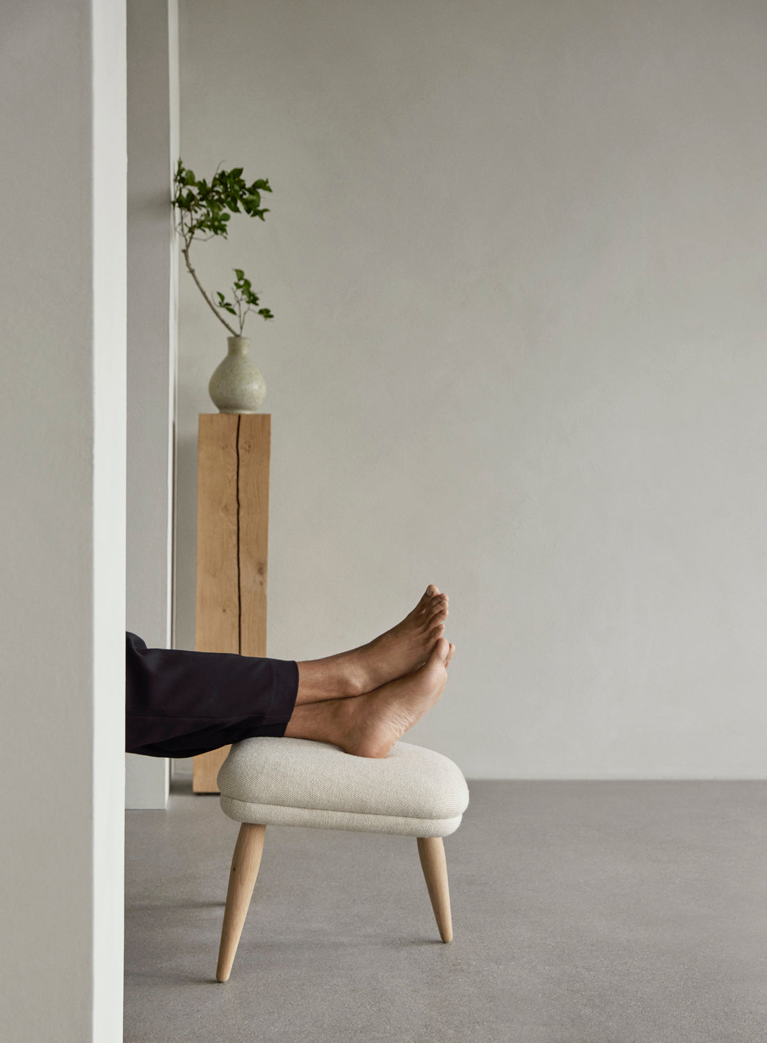 Cream upholstered round footstool with oak legs supporting a person's bare feet,