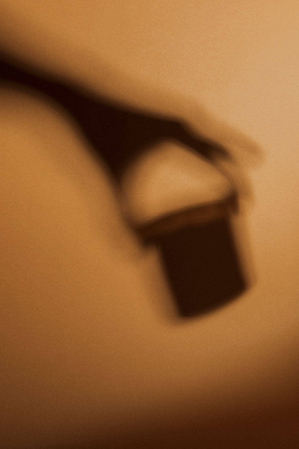 Blurry warm-toned shadow of a hand holding a small cylindrical lamp with