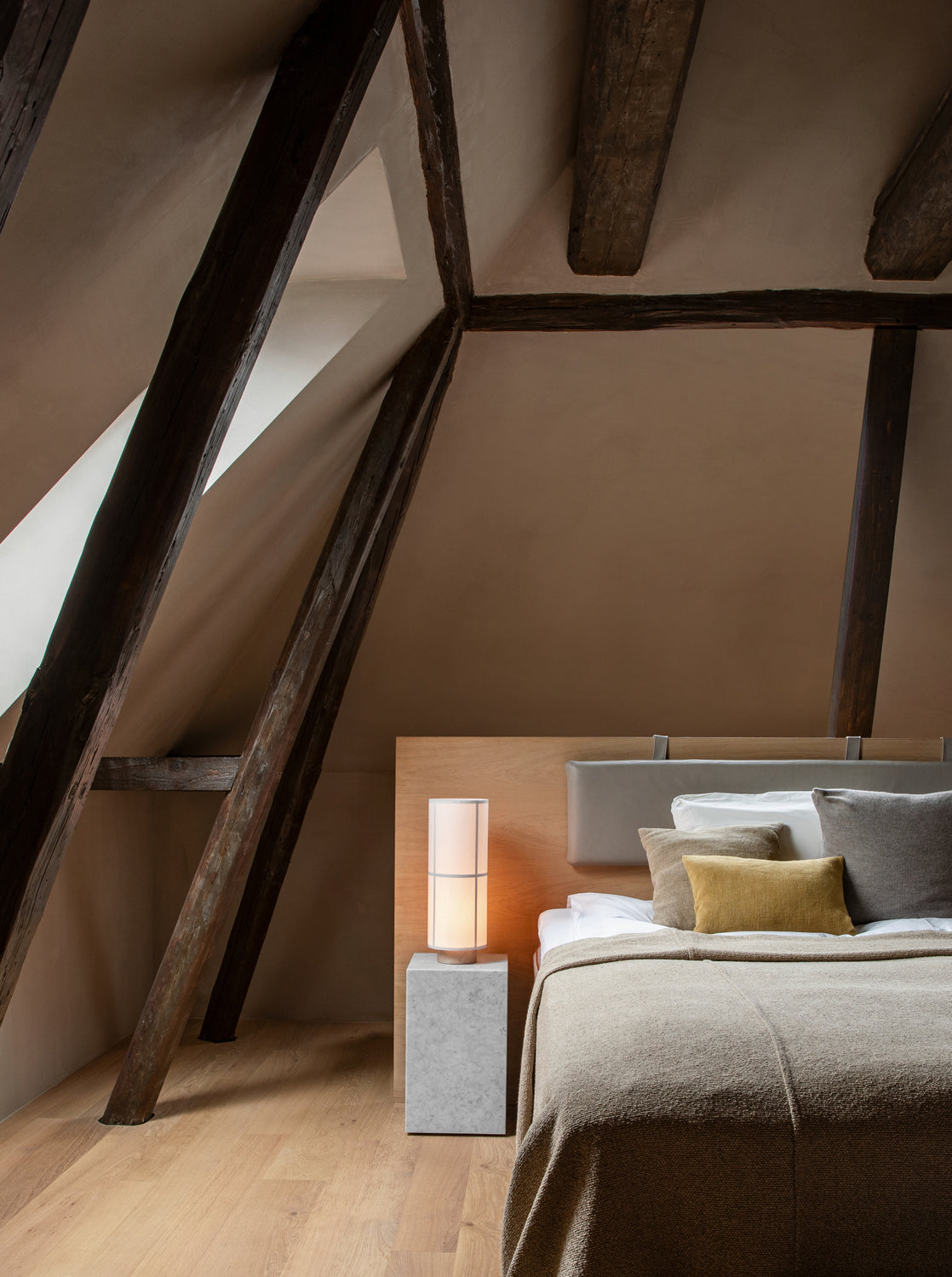 Minimal attic bedroom with exposed dark wooden beams, oak headboard, beige linen