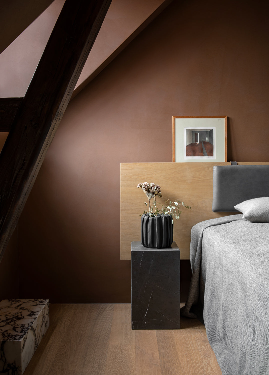 Minimal bedroom corner with brown plaster wall, oak headboard, black ribbed cera