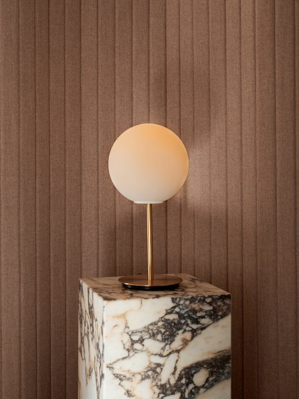 Brass table lamp with frosted white globe on a marble pedestal against