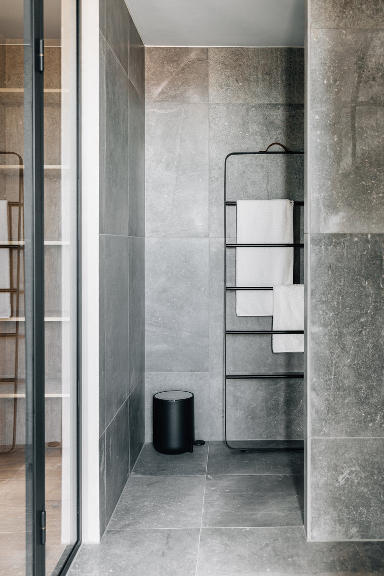 Minimal bathroom corner with large grey stone tiles, black cylindrical pedal bin