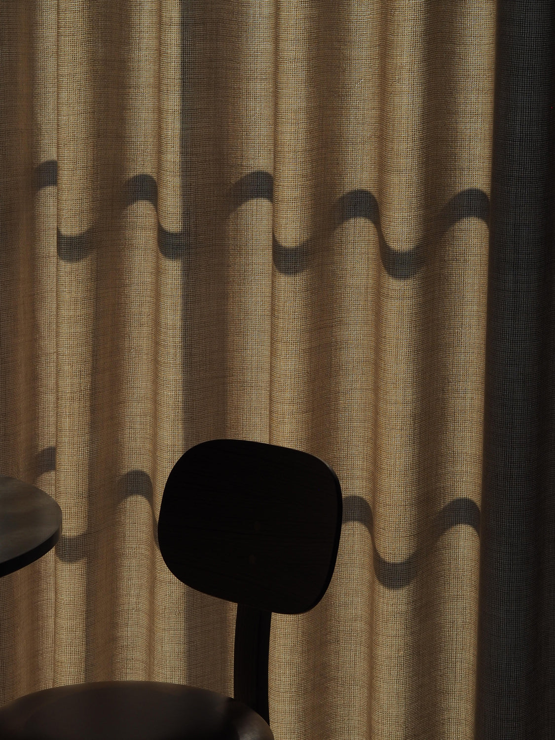 Beige textured linen curtain with dark wavy shadow pattern, partial silhouette o