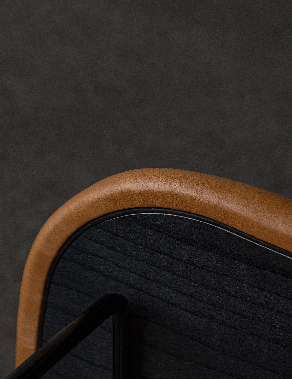 Close-up of a chair back with tan leather padded edge, black stained