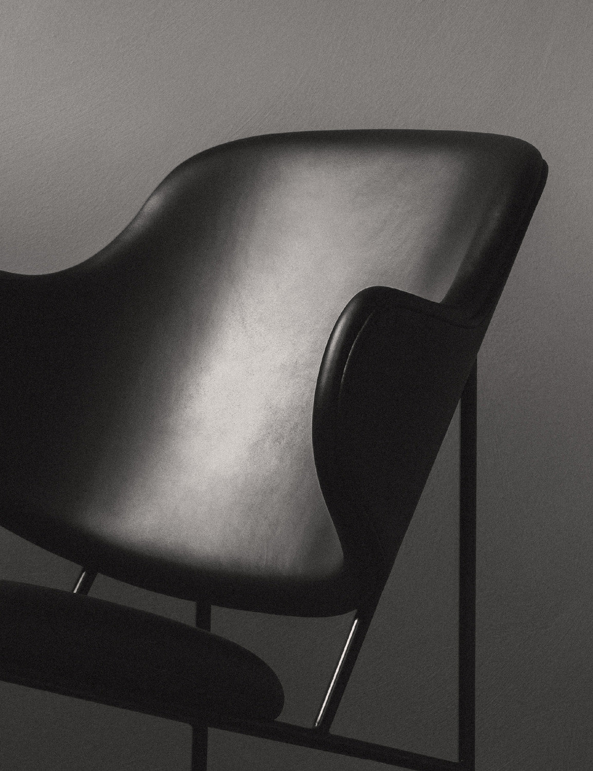Close-up of a black leather modern armchair with smooth curved backrest, slim