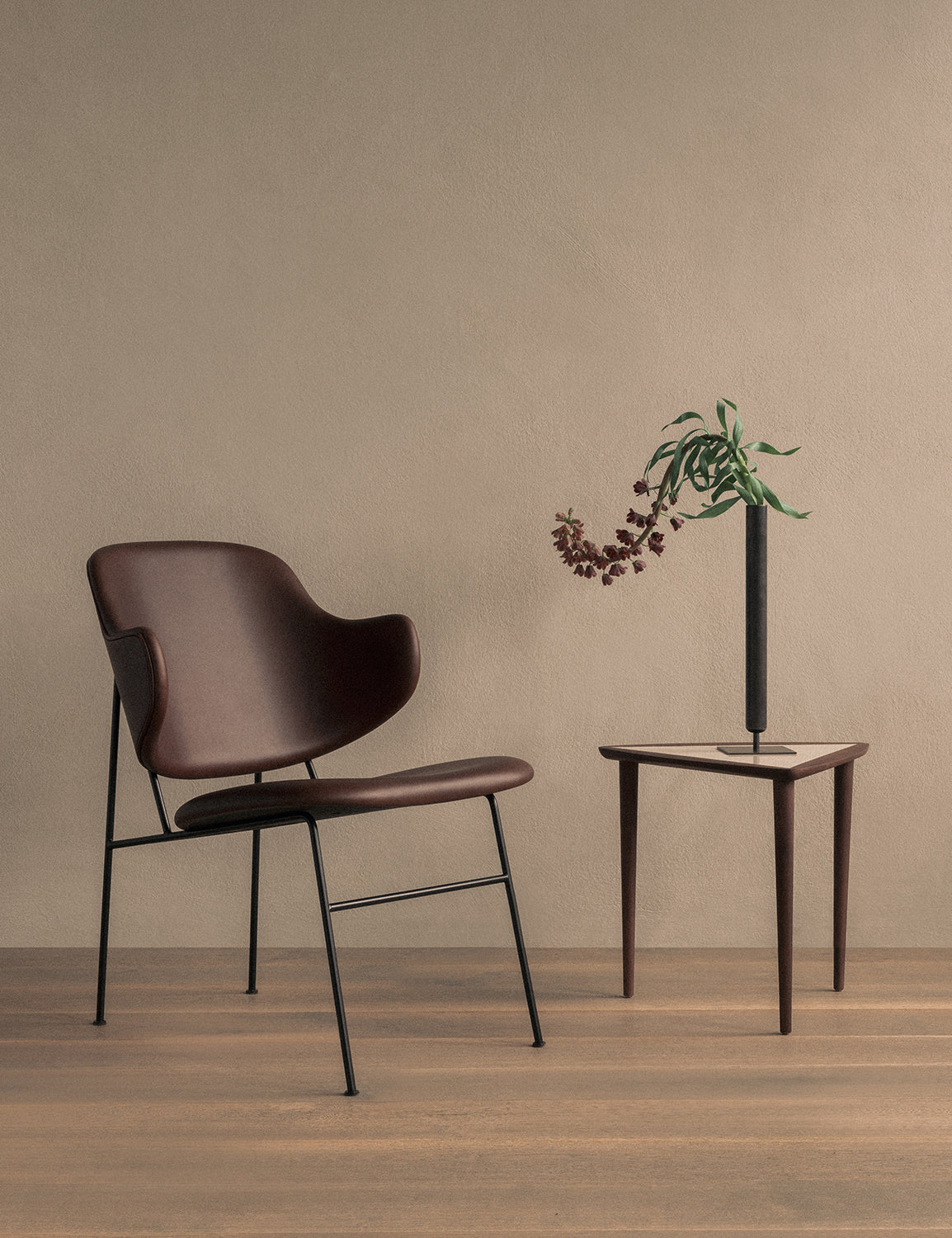 Brown leather lounge chair with thin black metal legs beside a triangular
