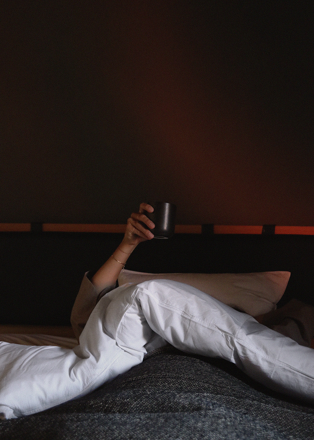 Hand holding matte black ceramic mug above white duvet and grey textured