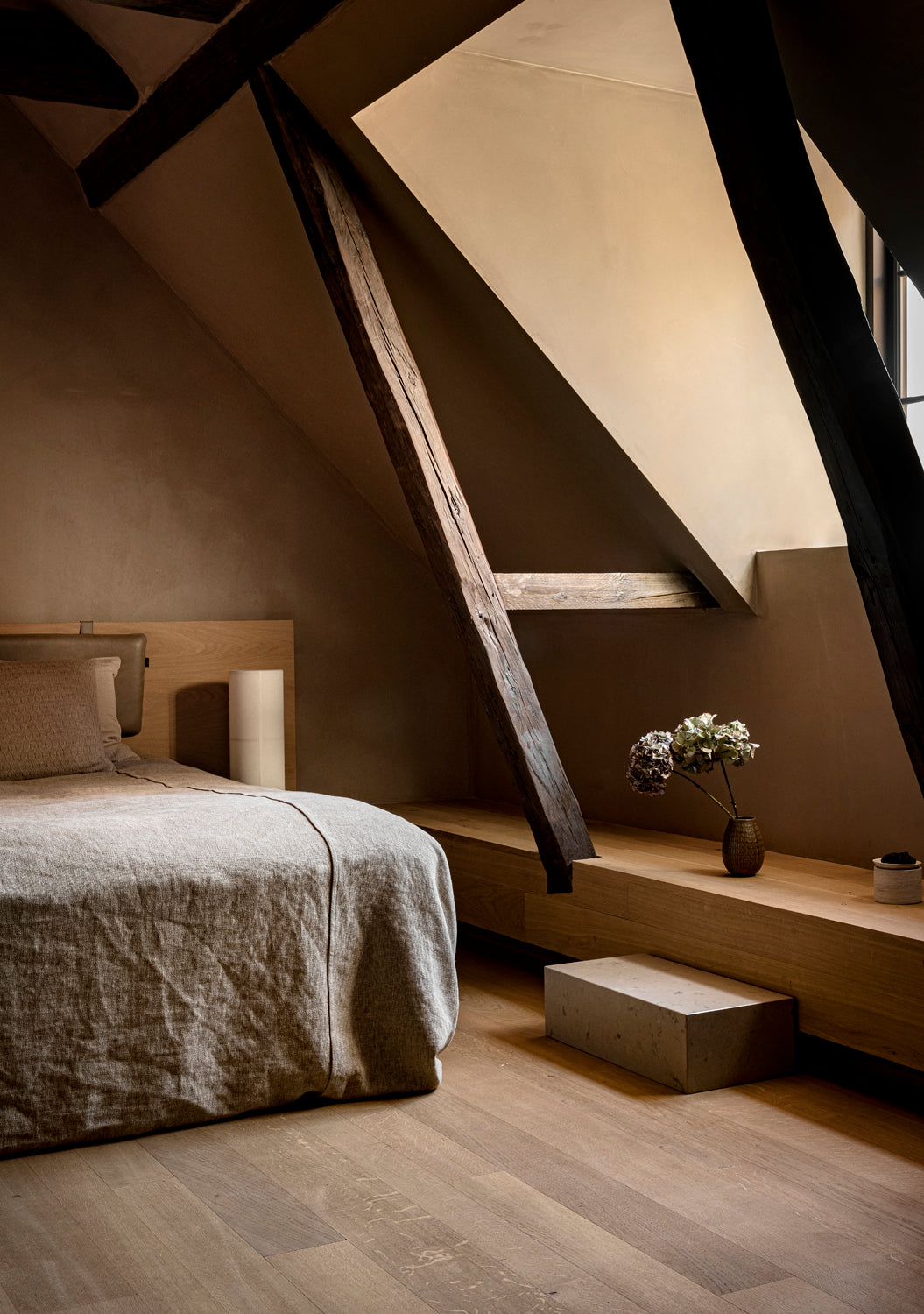 Minimal attic bedroom with slanted skylight, exposed dark wooden beams, oak plat