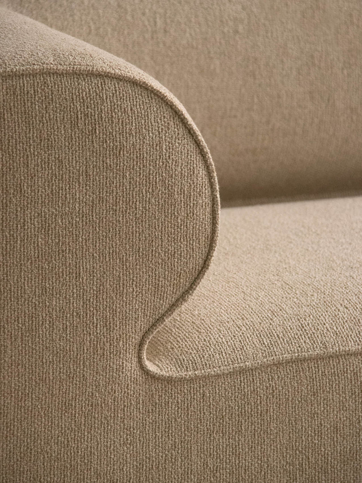 Close-up of beige boucle fabric armrest and seat with rounded piping detail