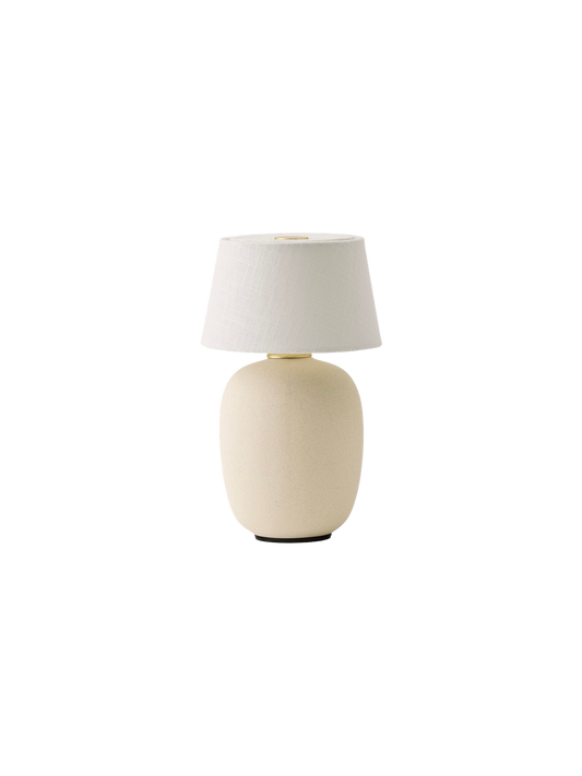 A Torso Portable Table Lamp in Sand, with a rounded, textured ceramic base and a white linen shade on a black background.