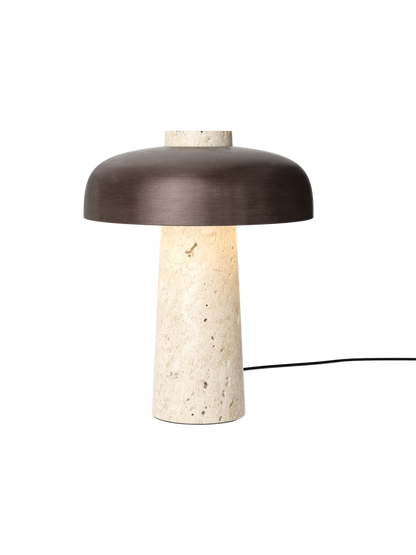 Front view of the Reverse Table Lamp with its lit, conical travertine base and a wide, curved bronzed aluminium shade.