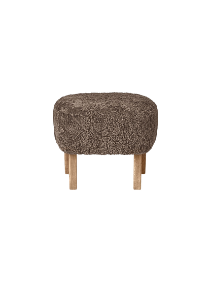 The oval Ingeborg Ottoman with a cushioned top upholstered in curly Sahara sheepskin on four short natural oak legs.